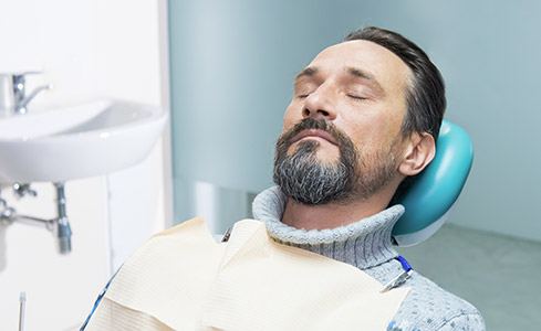 Man under IV dental sedation with eyes closed in dental chair