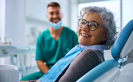 Woman smiling while sitting in treatment chair with dentist