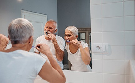 Couple smiling while brushing teeth together in bathroom