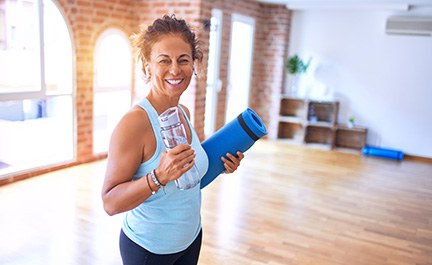 Woman smiling while holding water bottle and yoga mat